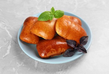Delicious baked pirozhki and basil on light grey marble table