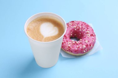 Tasty frosted donut and paper cup of coffee on light blue background