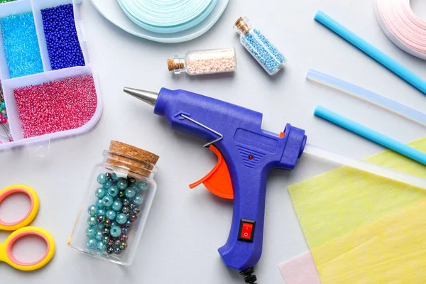 Hot glue gun and handicraft materials on grey background, flat lay