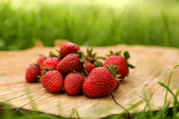 Pile of delicious ripe strawberries on tree stump outdoors, closeup