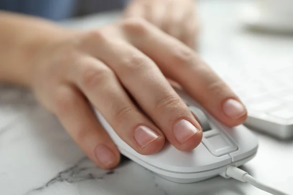 Woman using wired computer mouse at marble table, closeup