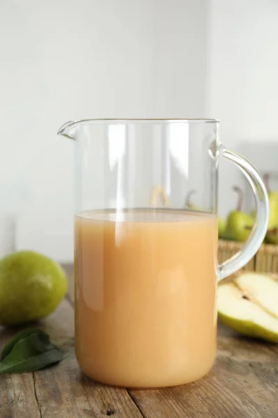 Fresh pear juice in glass jug on wooden table, closeup