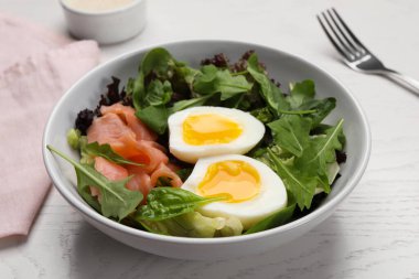 Delicious salad with boiled egg, salmon and arugula on white wooden table, closeup