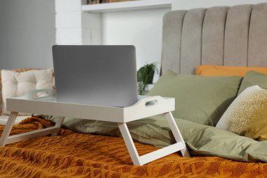 Beyaz tepsi ve yatağın içinde modern laptop var.