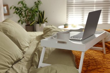 White tray with modern laptop and cup of aromatic drink on bed indoors, space for text