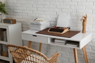 Comfortable writer's workplace with typewriter on desk near white brick wall