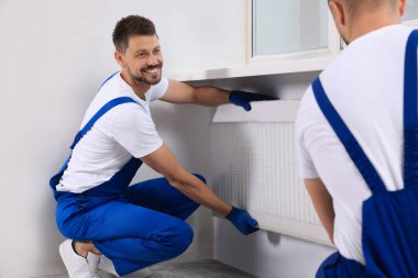 Professional plumbers installing new heating radiator in room