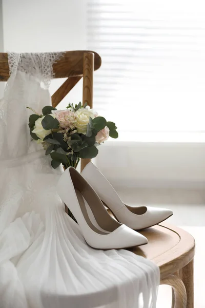 White high heel shoes, flowers and wedding dress on wooden chair indoors