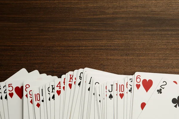Deck of playing cards on wooden table, top view. Space for text