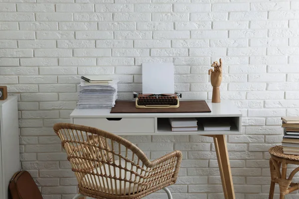 Comfortable writer's workplace with typewriter on desk near white brick wall