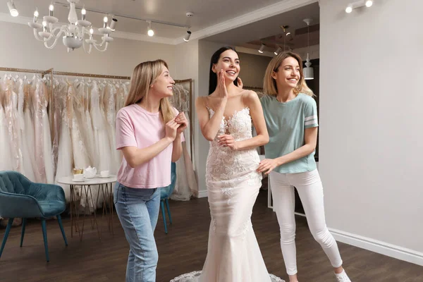 Bride with friends choosing wedding dress in boutique