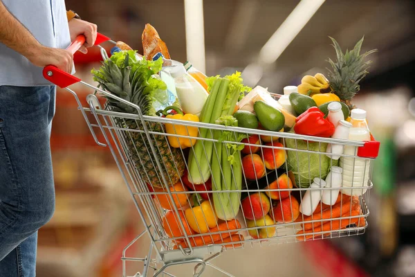 Man with shopping cart full of groceries in supermarket, closeup