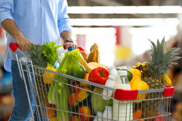 Man with shopping cart full of groceries in supermarket, closeup