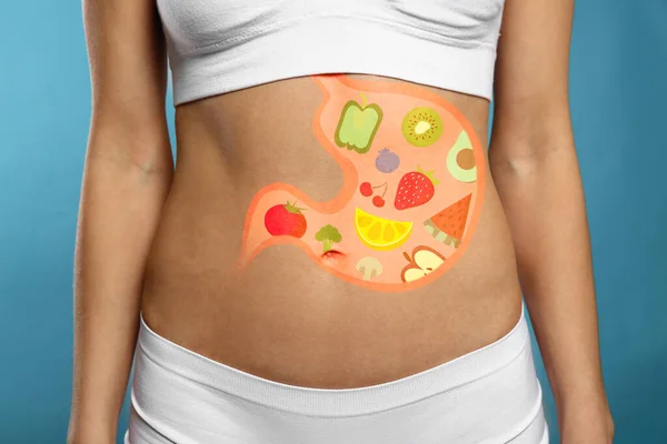 Woman with image of stomach full of food drawn on her belly against light blue background, closeup. Healthy eating habits