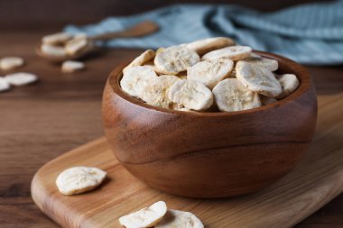 Bowl and dried banana slices on wooden table, closeup