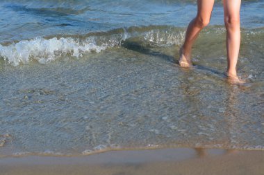 Child walking through water on seashore, closeup of legs