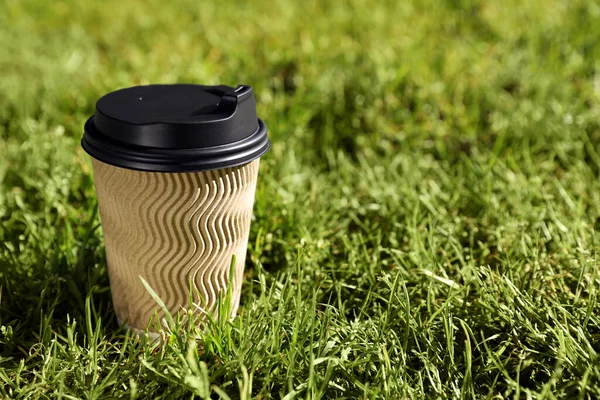 Cardboard takeaway coffee cup with plastic lid on green grass outdoors, space for text
