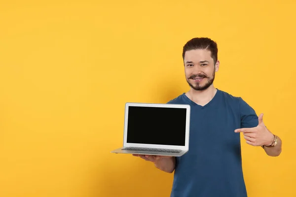Emotional man pointing at laptop on orange background. Space for text