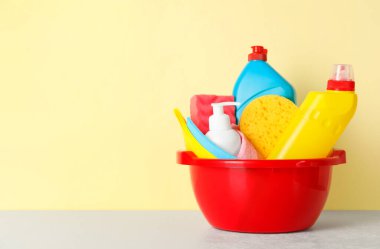 Basin with different cleaning supplies on light floor near beige wall. Space for text