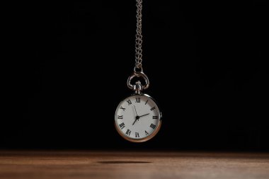 Beautiful vintage pocket watch with silver chain on black background above wooden table. Hypnosis session