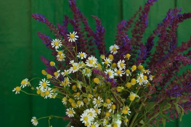 Beautiful bouquet with field flowers near green wooden wall, closeup