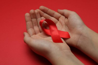 Küçük kız parlak arka planda kırmızı kurdele tutuyor, yakın plan. AIDS Hastalığı Farkındalığı