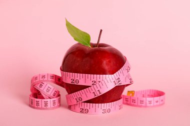 Fresh red apple with measuring tape on pink background