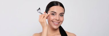 Beautiful young woman with eyelash curler on white background. Banner design
