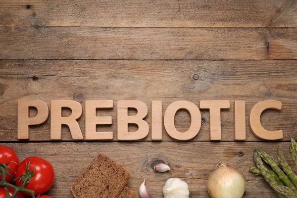 Word Prebiotic made of letters and foodstuff on wooden table, flat lay. Space for text