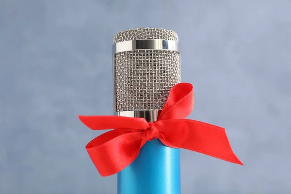 Microphone with red bow on grey background, closeup. Christmas music