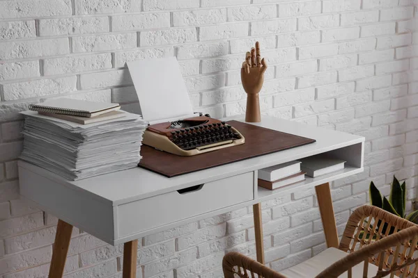 Comfortable writer\'s workplace with typewriter on desk near white brick wall