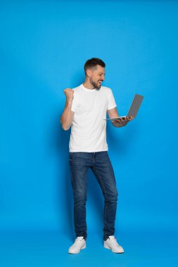 Happy man looking at laptop on light blue background