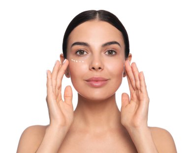 Beautiful young woman with cream on skin under eye against white background