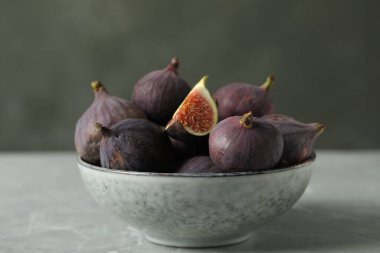 Tasty raw figs in bowl on light grey marble table, closeup