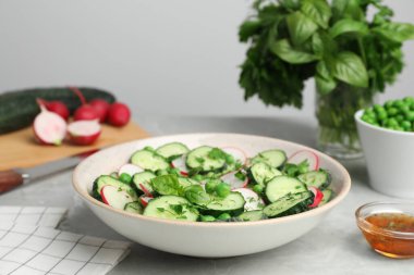 Appetizing salad with cucumbers, radish and pea in bowl served on light grey table