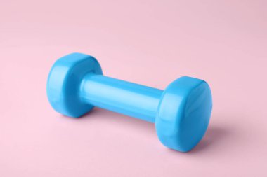 One turquoise dumbbell on light pink background