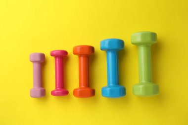 Many different stylish dumbbells on yellow background, flat lay