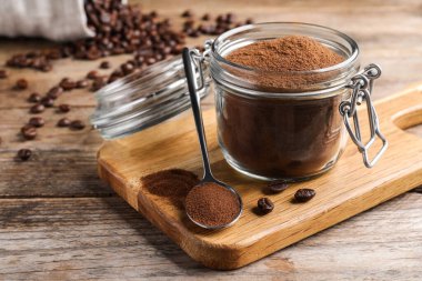 Glass jar of instant coffee and spoon on wooden table, closeup