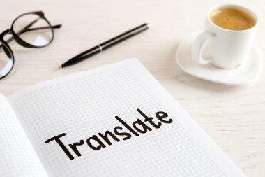 Notebook with written word Translate, pen, eyeglasses and cup of coffee on white wooden table