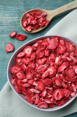 Bowl and spoon with dried strawberries on light blue wooden table, flat lay