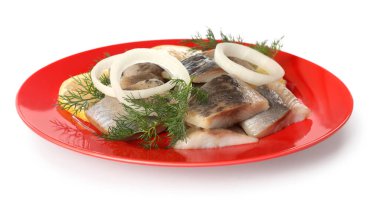 Red plate with delicious salted herring slices, onion rings and dill isolated on white