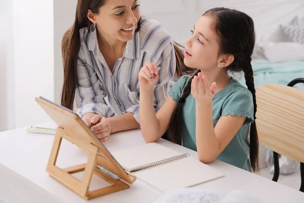 Mother helping her daughter doing homework with tablet at home