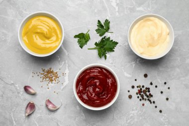 Bowls with mustard, ketchup and mayonnaise on light grey table, flat lay