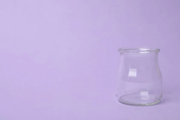 Open empty glass jar on lilac background, space for text