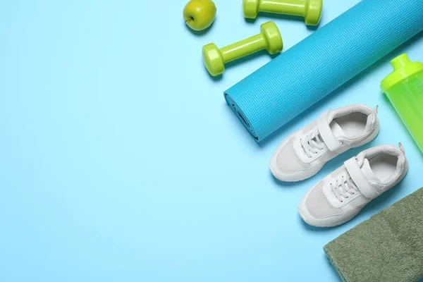 Exercise mat, dumbbells, apple, towel, shaker and shoes on light blue background, flat lay. Space for text