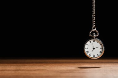 Beautiful vintage pocket watch with silver chain on black background above wooden table, space for text. Hypnosis session