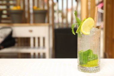 Glass of refreshing citrus drink on white table in cafe, space for text