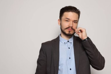 Handsome man in suit touching mustache on light grey background. Space for text