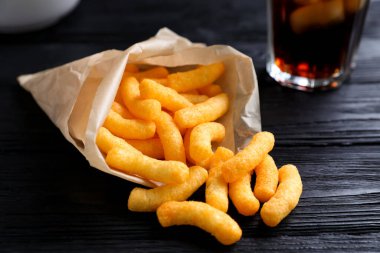Crunchy cheesy corn snack on black wooden table, closeup