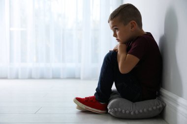 Sad little boy near white wall indoors, space for text. Domestic violence concept